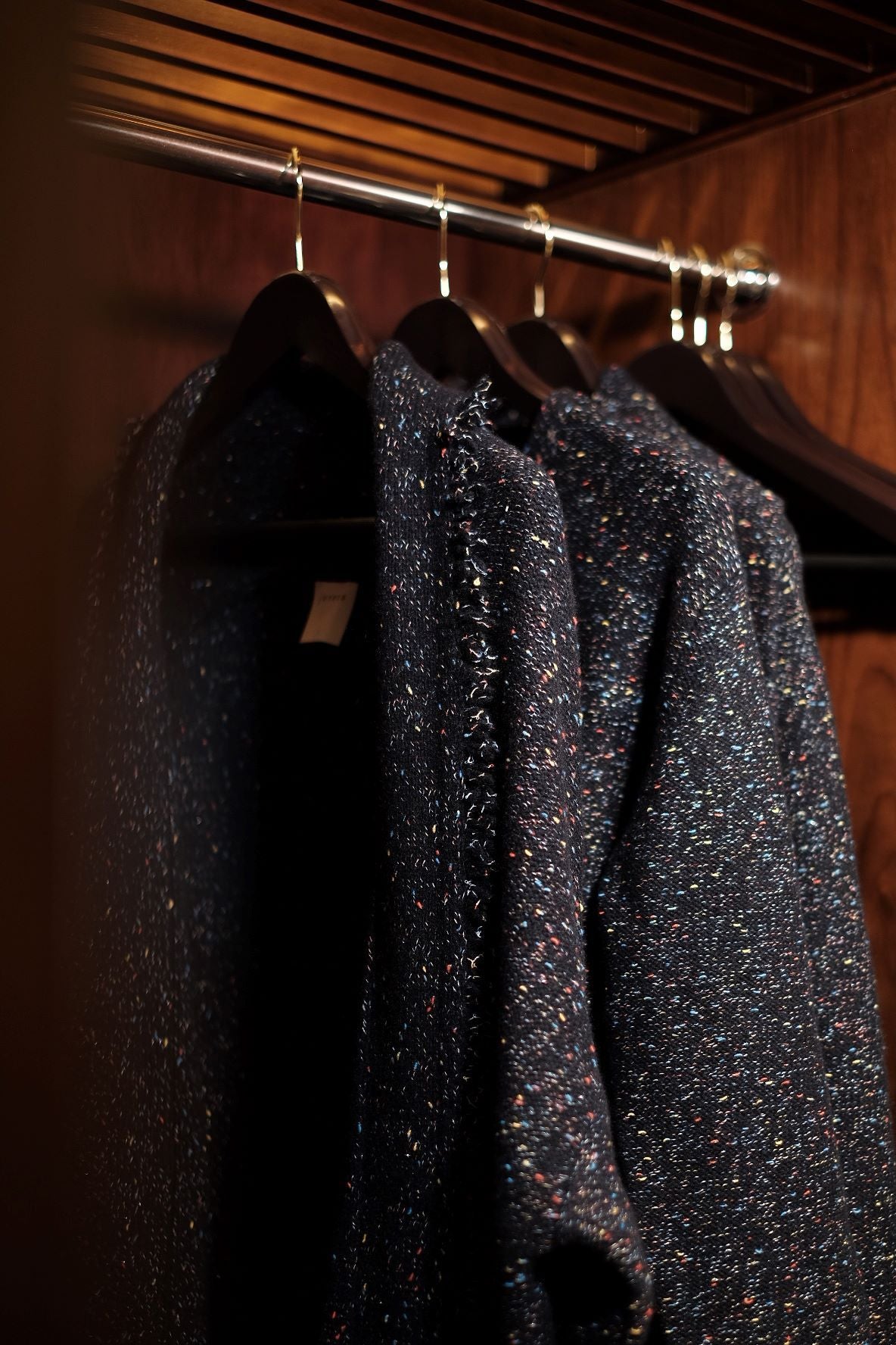 Two dark gray textured coats hanging on a rack with a wooden background
